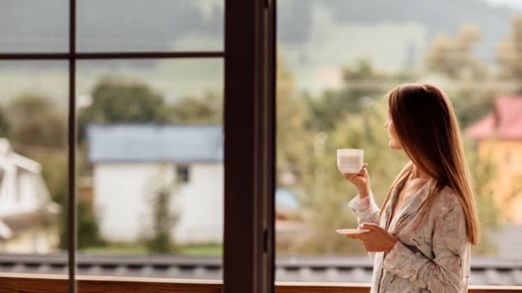 woman morning holding cup tea coffee looking mountains standing near window cropped 28