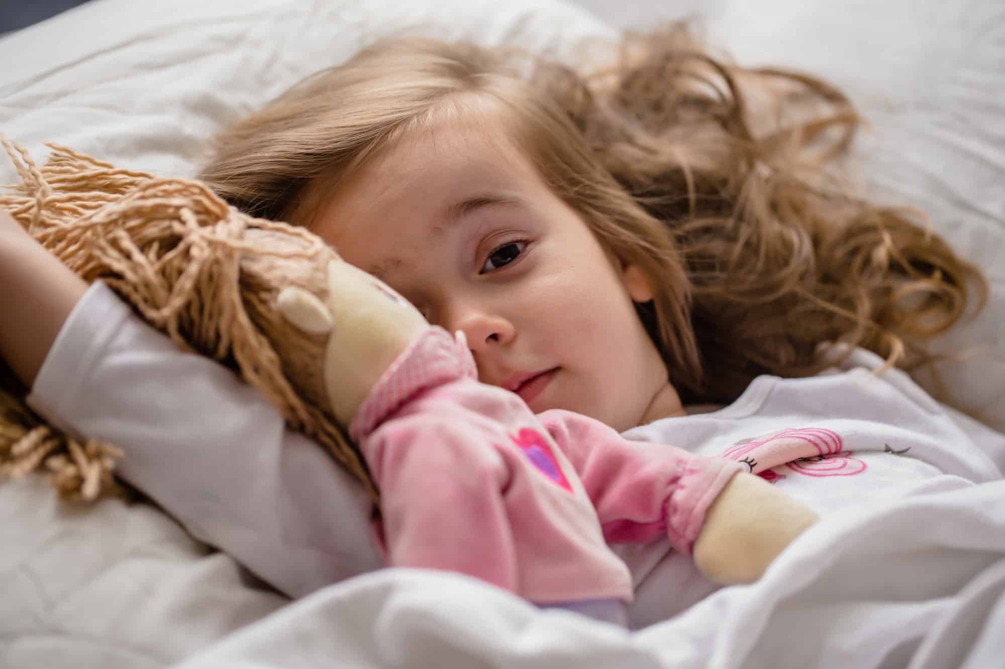 little girl falls asleep in bed with soft doll white